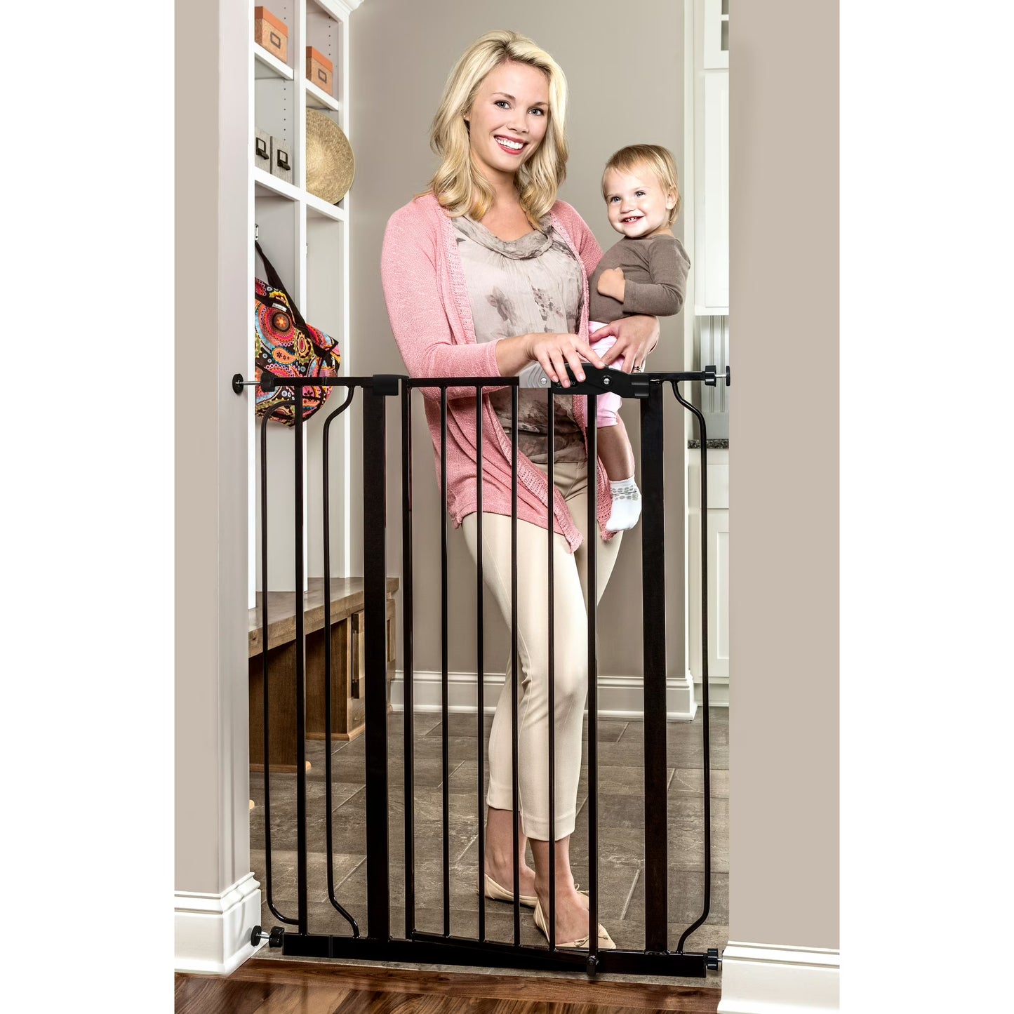 Woman holding a child next to a black metal gate in a home setting