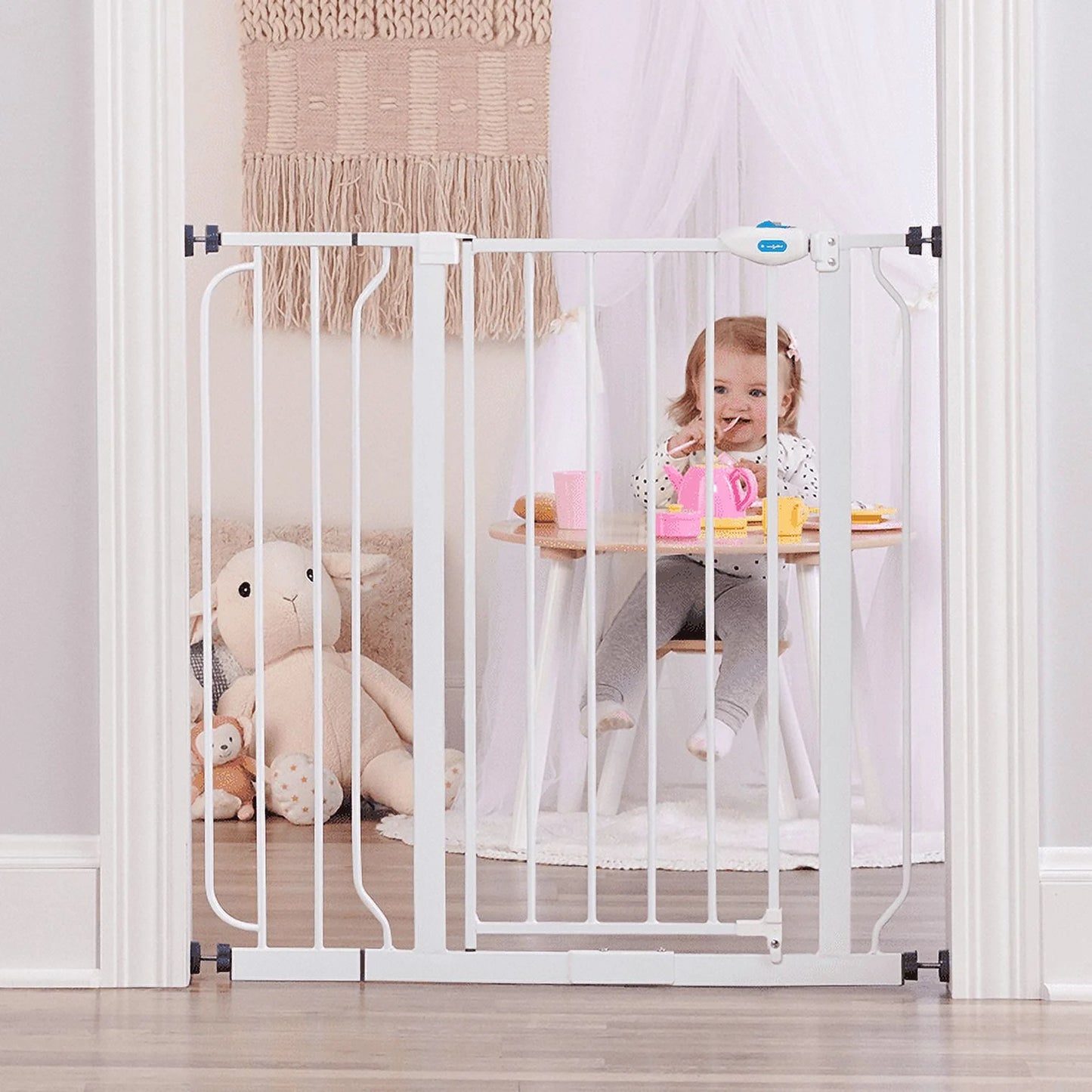 Child sitting at a table behind a white baby gate in a room with toys and a rug.