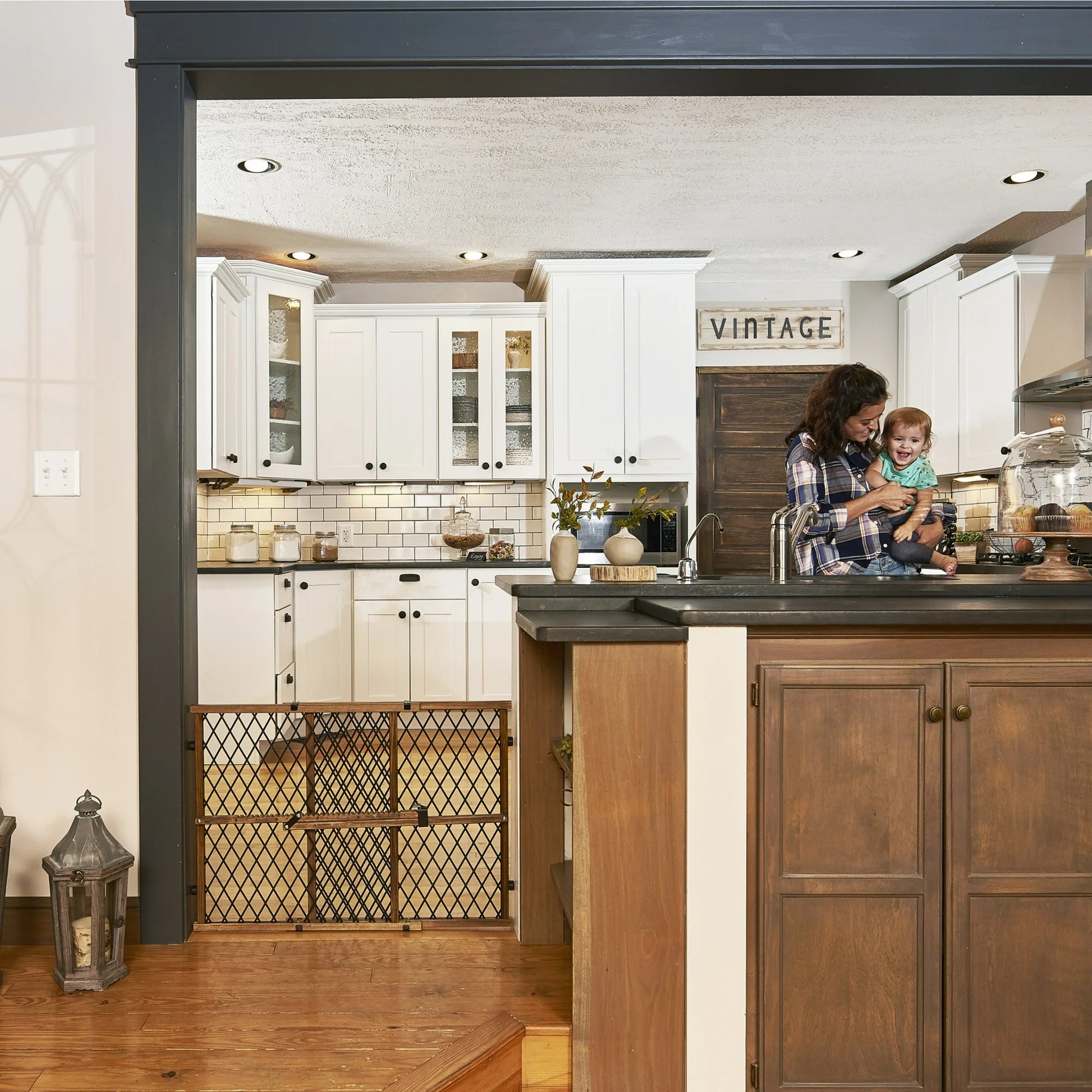 Woman holding a child in a modern kitchen with white and wooden cabinets.