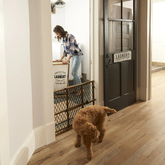Woman in plaid shirt and jeans standing in a laundry room with a dog on a wooden floor.
