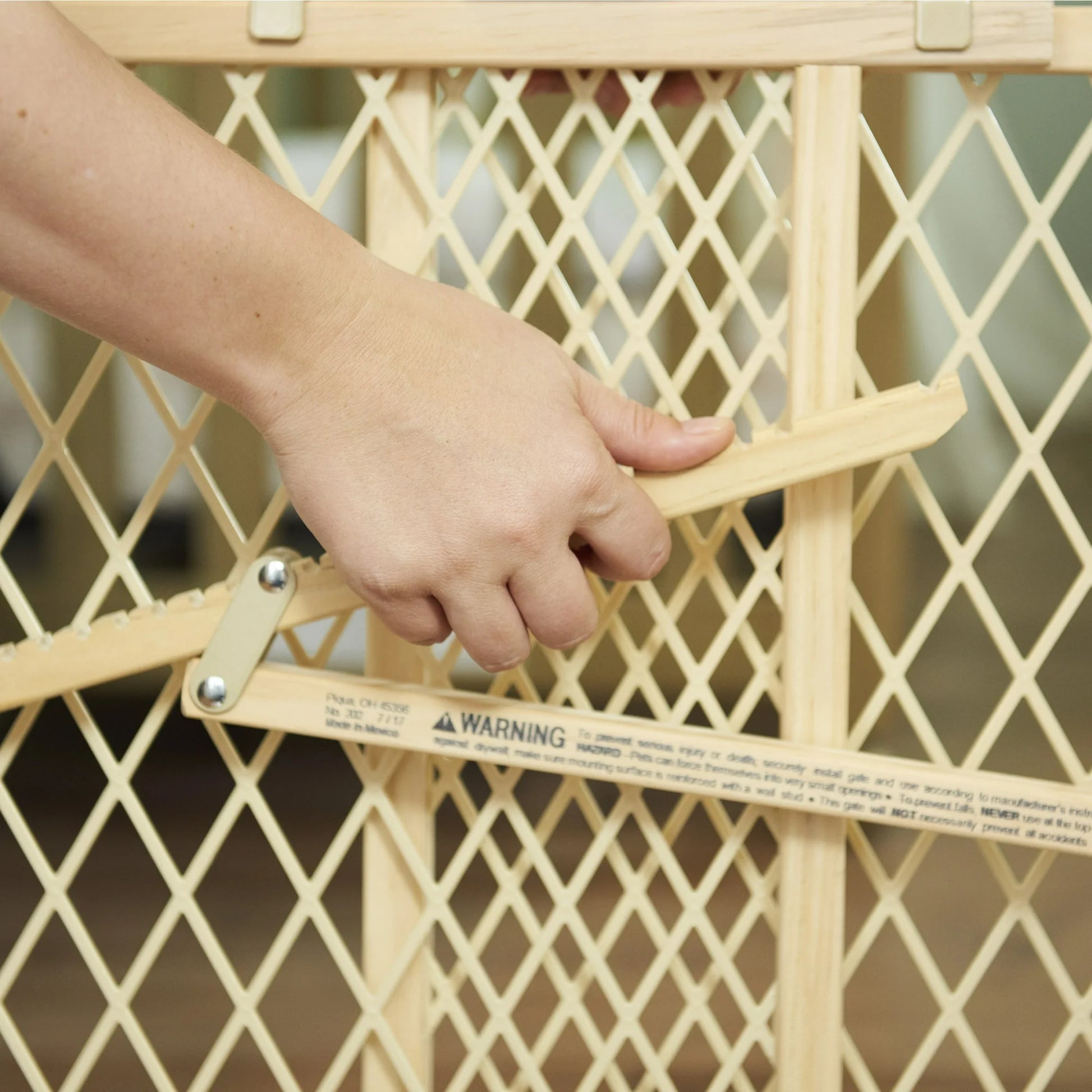Hand adjusting a beige baby gate with a warning label.
