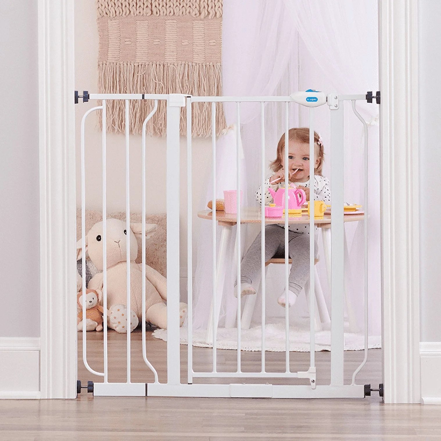 Child sitting at a table behind a white baby gate in a room with toys and a rug.